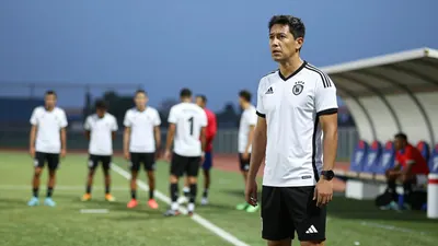 A 30-year-old Necaxa coach, wearing a white jersey with a black stripe, and a black pair of shorts, stands on the...