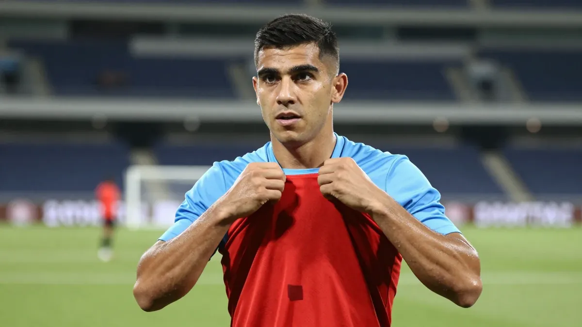 A close medium shot fills the frame with a Necaxa first-team player in his late twenties, jawline sharp, eyes locked on...