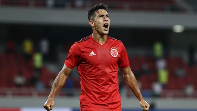 Photorealistic 85mm f/1.4 shot of a muscular 22-year-old Colombian striker in solid red kit, mid-celebration after...