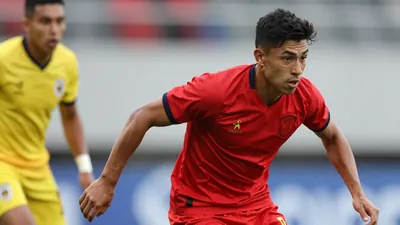 A tight action shot of a young, muscular Mexican forward in a red jersey, mid-dribble against a defender in a yellow jersey