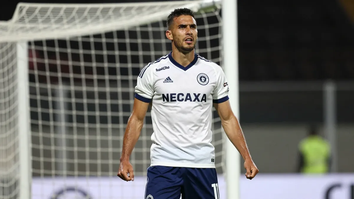 Waist-up shot of a muscular, 26-year-old forward wearing a Club Necaxa kit with deep blue shorts and a white jersey...