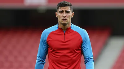 Mid-30s, muscular forward, shoulders hunched, eyes glistening with disappointment, wearing a plain red and sky-blue...